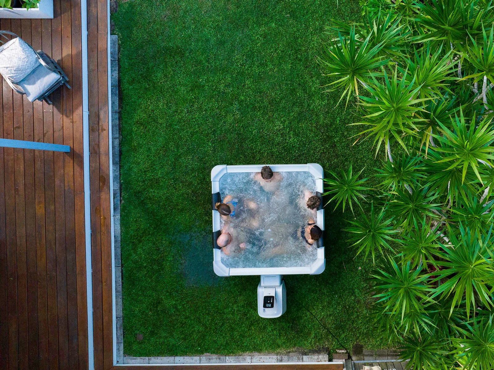 Dört kişinin bahçede jakuzi keyfi, yeşil çim ve dış mekan mobilyası yanlarında