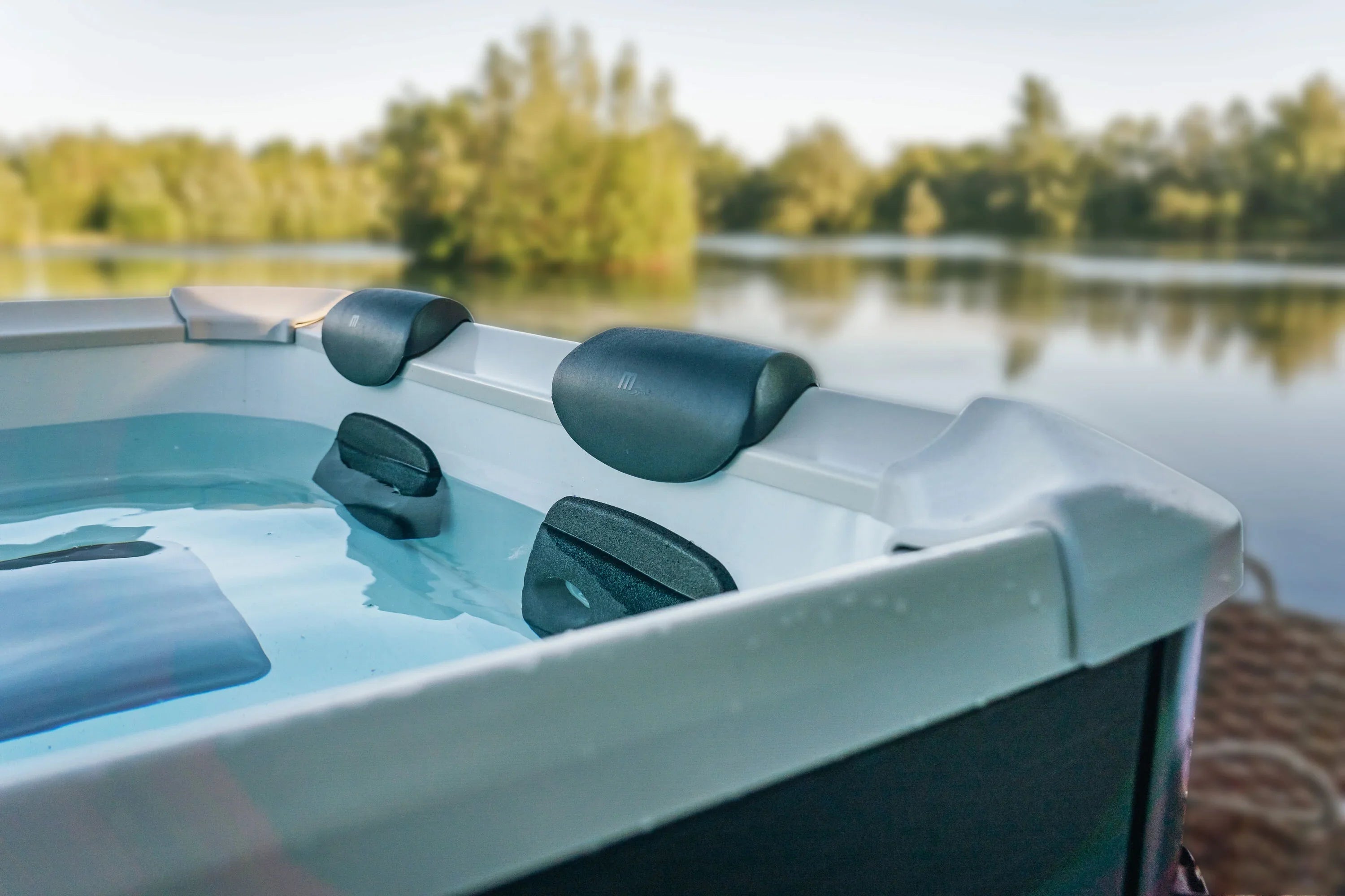 Göl manzaralı dış mekanda beyaz jakuzi içinde siyah yastıklı rahat oturma alanı