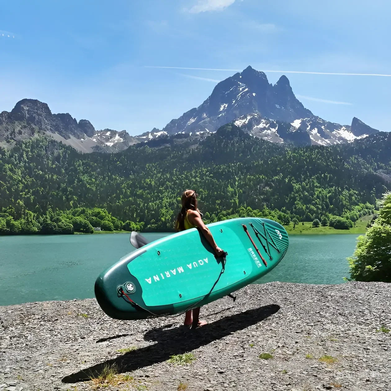 Dağ manzaralı göl kenarında Aqua Marina şişme paddleboard taşıyan kadın