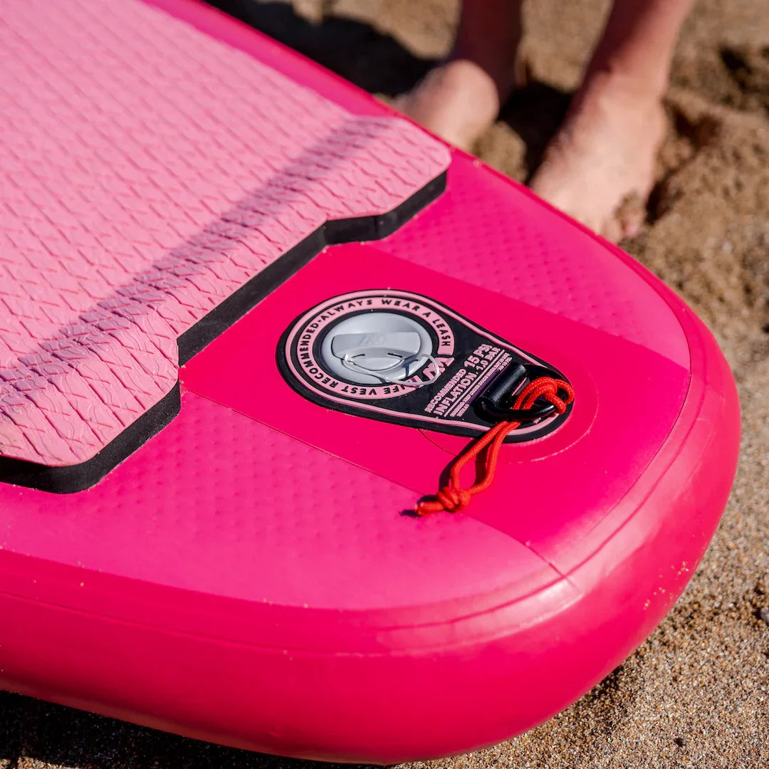 Close-up of bright raspberry pink Aqua Marina Coral stand-up paddleboard leash attachment on sandy beach