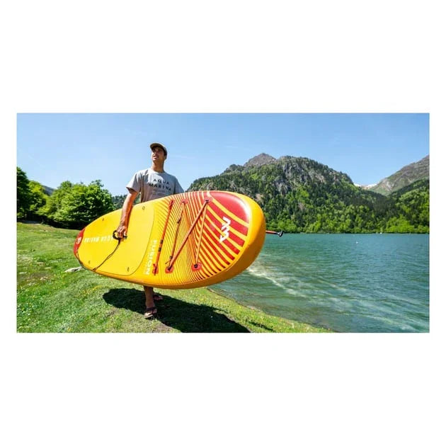 Dağ manzaralı göl kenarında sarı-kırmızı Aqua Marina Fusion şişme stand up paddle board taşıyan adam