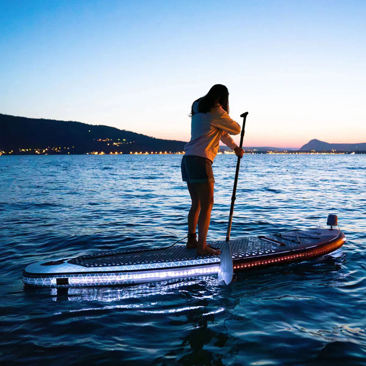 Person paddleboarding on illuminated stand-up paddleboard at sunset on calm water