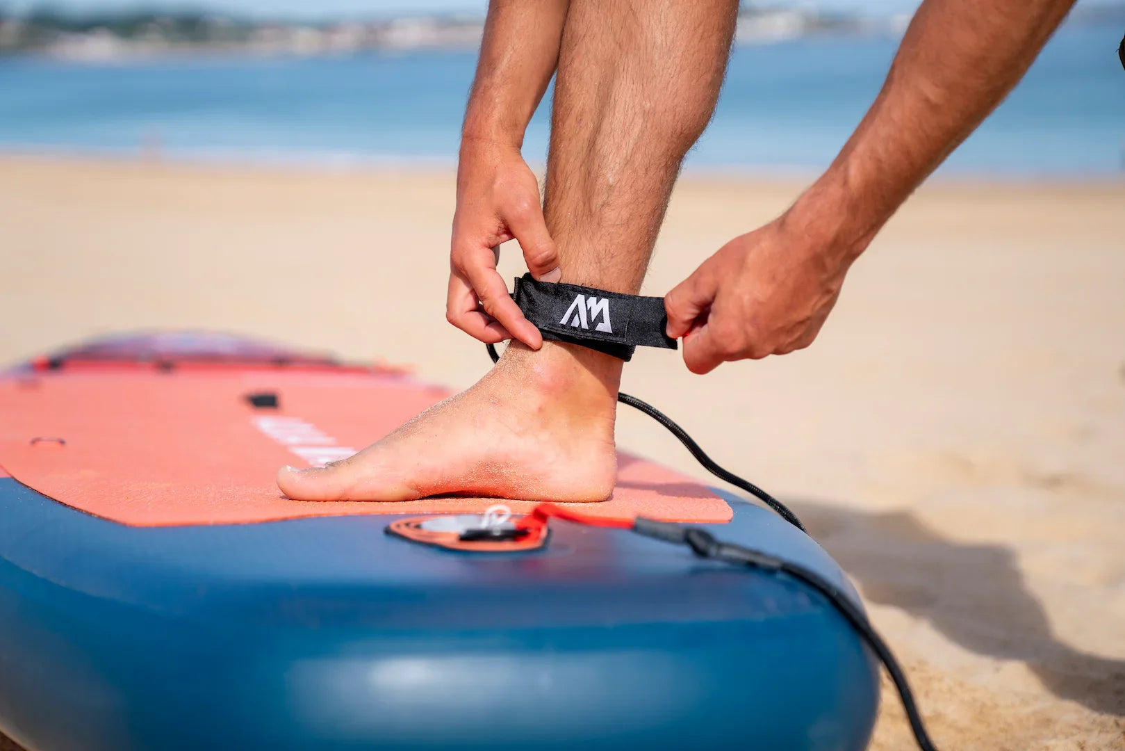 Deniz kıyısında Aqua Marina Monster şişme isup üzerinde ayak bileğine kurulan siyah kayışlı paddle board bağlaması