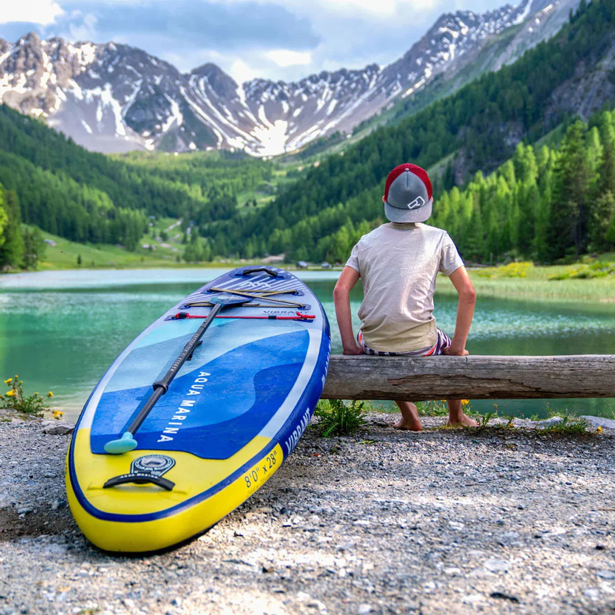 Dağ manzarasında göl kenarında oturan çocuk ve Aqua Marina Vibrant şişme stand up paddle board